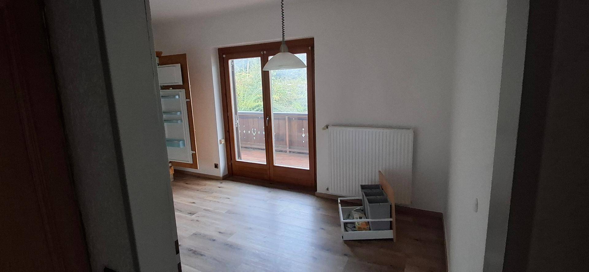 Heller Wohnbereich mit Laminatboden und Zugang zu einem Balkon, ideal für entspannte Stunden.