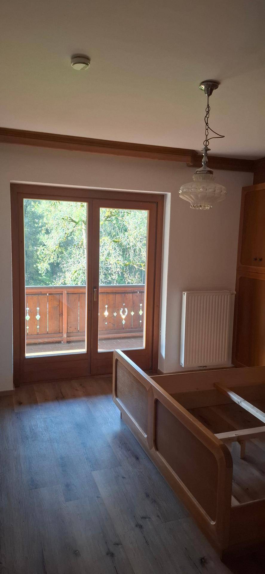 Helles Schlafzimmer mit Balkonzugang und Blick ins Grüne, ausgestattet mit Laminatboden.