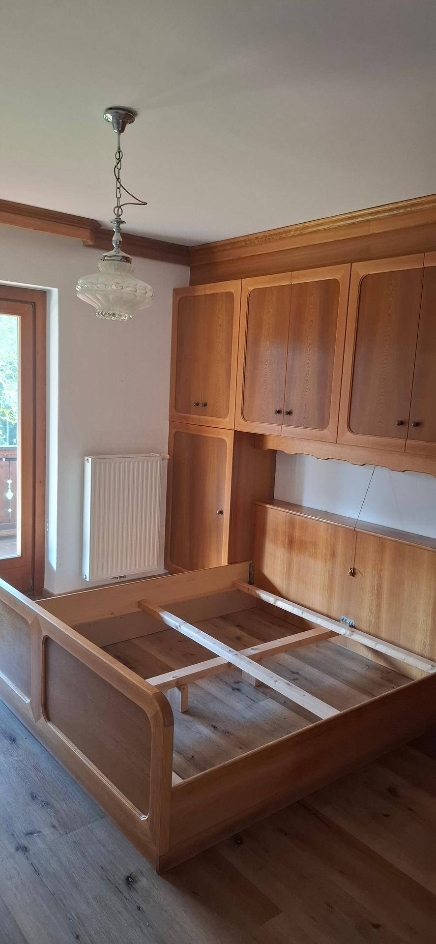 Schlafzimmer mit Holzbett und Einbauschränken, die direkten Zugang zum Balkon ermöglichen.