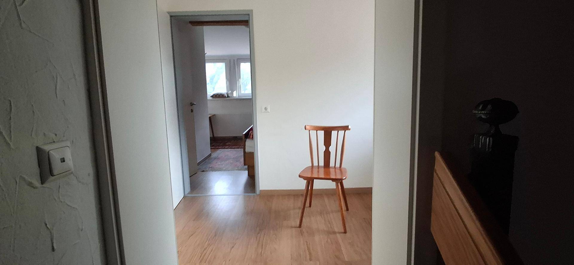 Heller Flur mit Laminatboden und einem Stuhl, der zu weiteren Räumen führt.