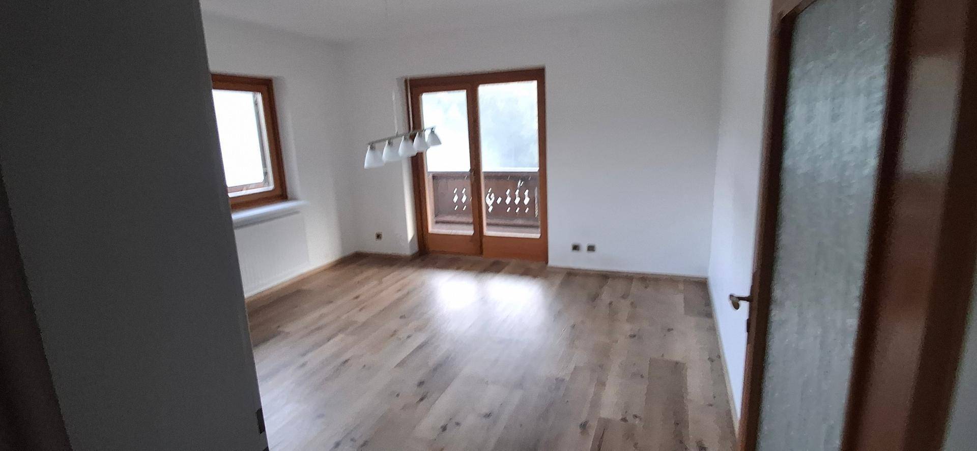 Helles Wohnzimmer mit Laminatboden und Balkonzugang, das viel Tageslicht erhält.