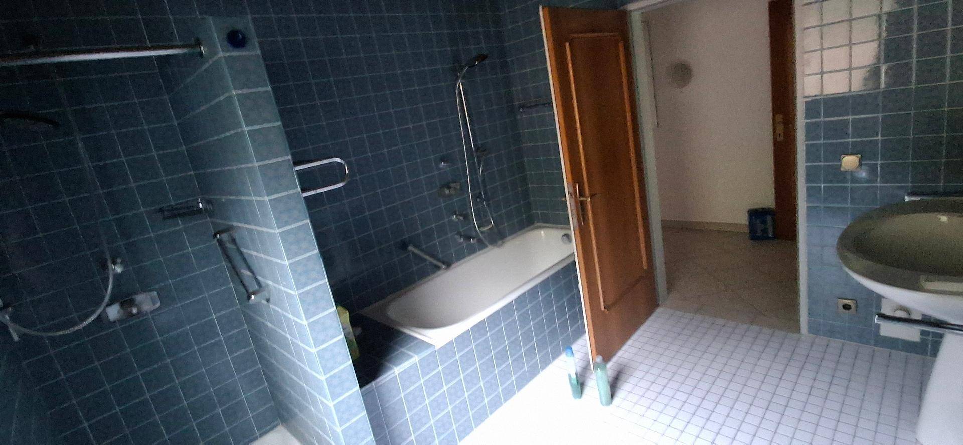 Badezimmer mit blauen Fliesen, Badewanne und Duschvorrichtung, die eine funktionale Ausstattung bietet.
