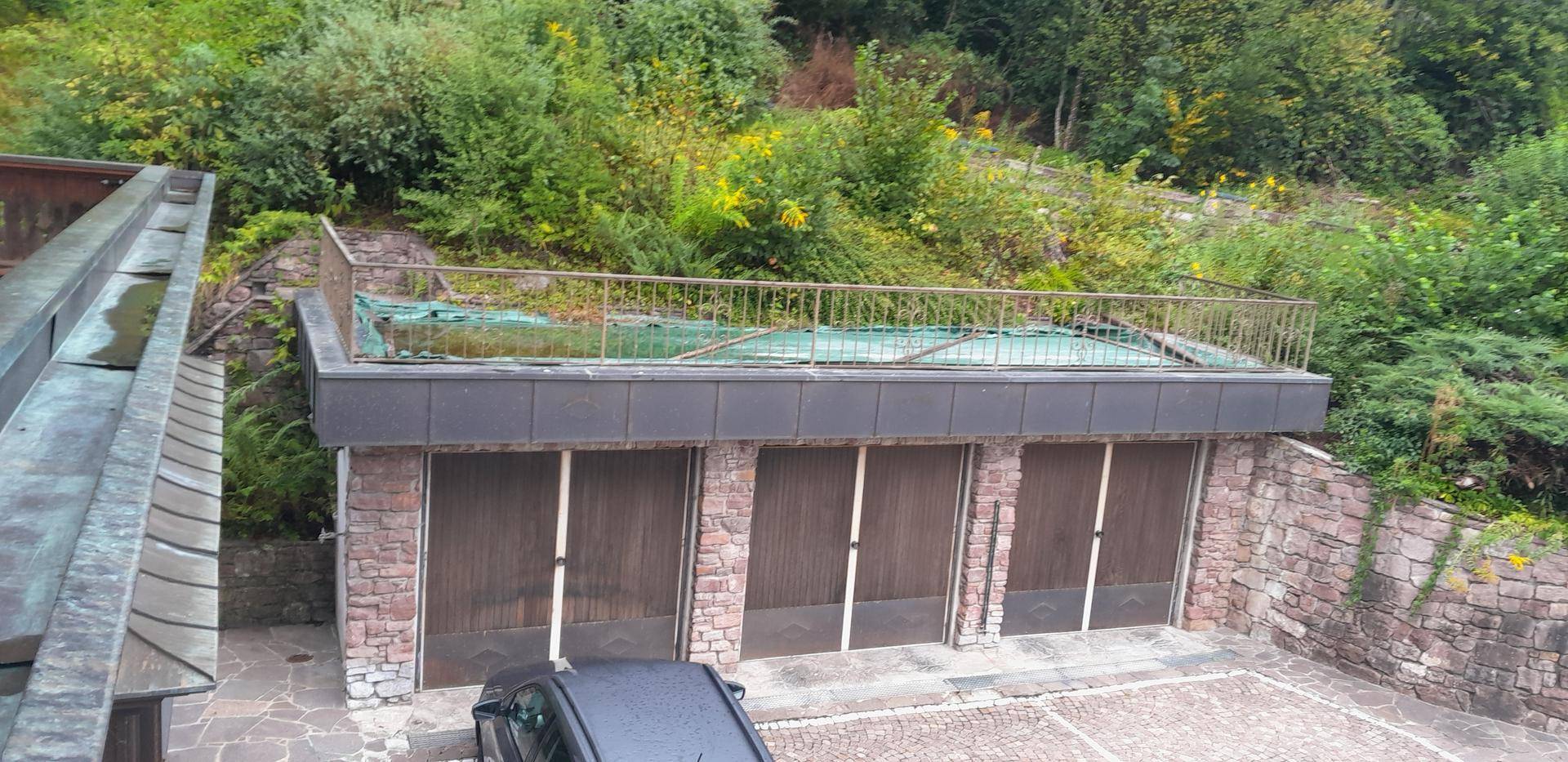 Garagengebäude mit drei Stellplätzen und begrüntem Flachdach, umgeben von üppiger Vegetation am Hang.