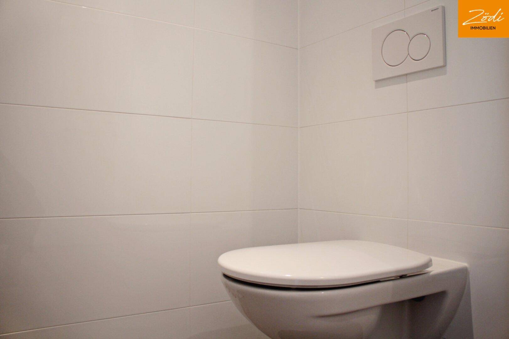 Sauberes WC mit wandmontierter Toilette und weißen Fliesen an den Wänden.