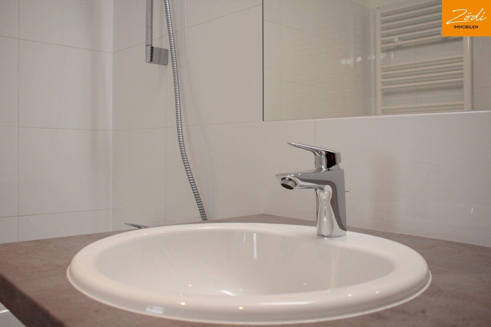 Modernes Badezimmer mit weißem Waschbecken, Chromarmatur und Duschbereich.