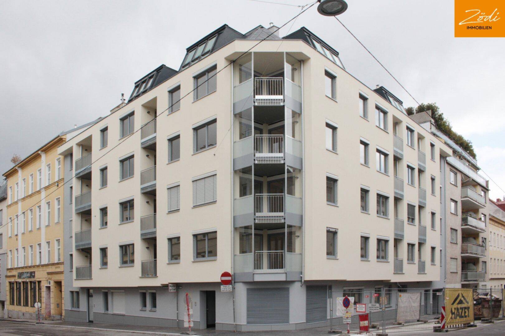 Modernes Eckgebäude mit mehreren Balkonen und großen Fenstern in städtischer Umgebung.