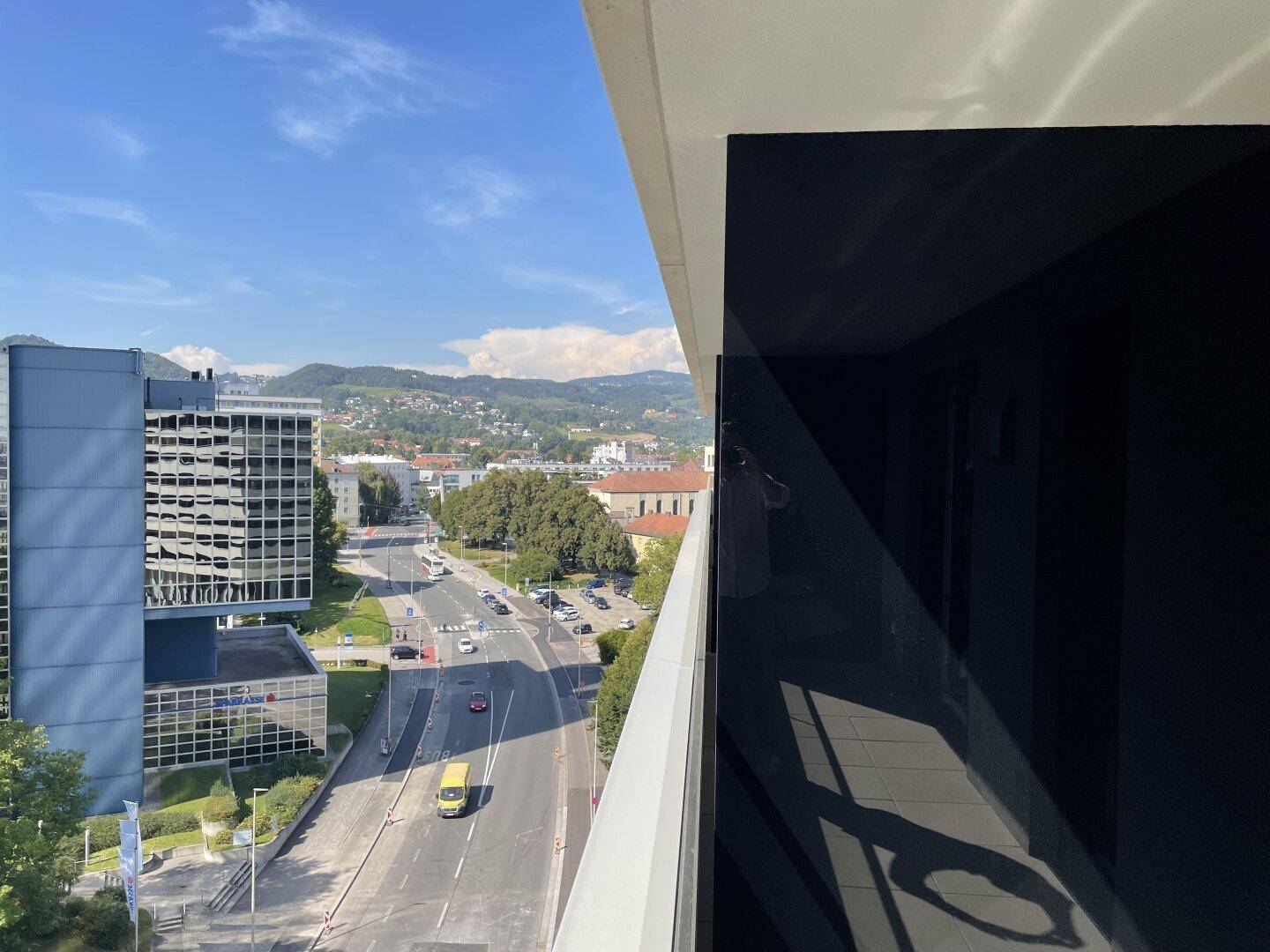 Weitblick von einem Balkon über die Stadt mit Bergen im Hintergrund.
