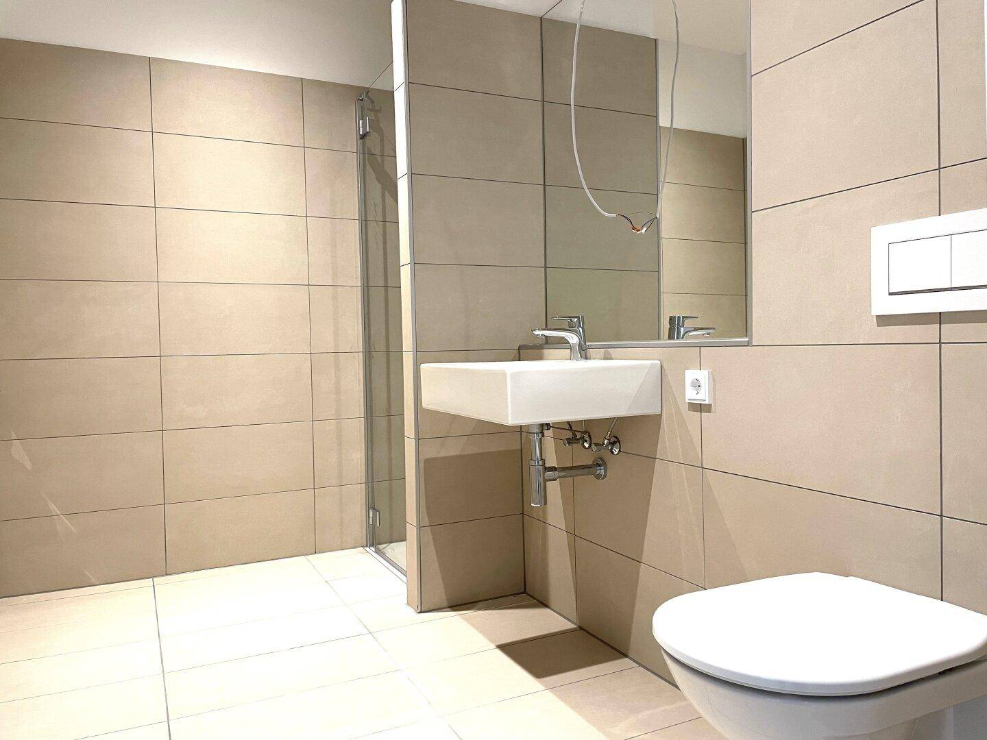 Modernes Badezimmer mit beigefarbenen Fliesen, Waschbecken und Duschbereich.