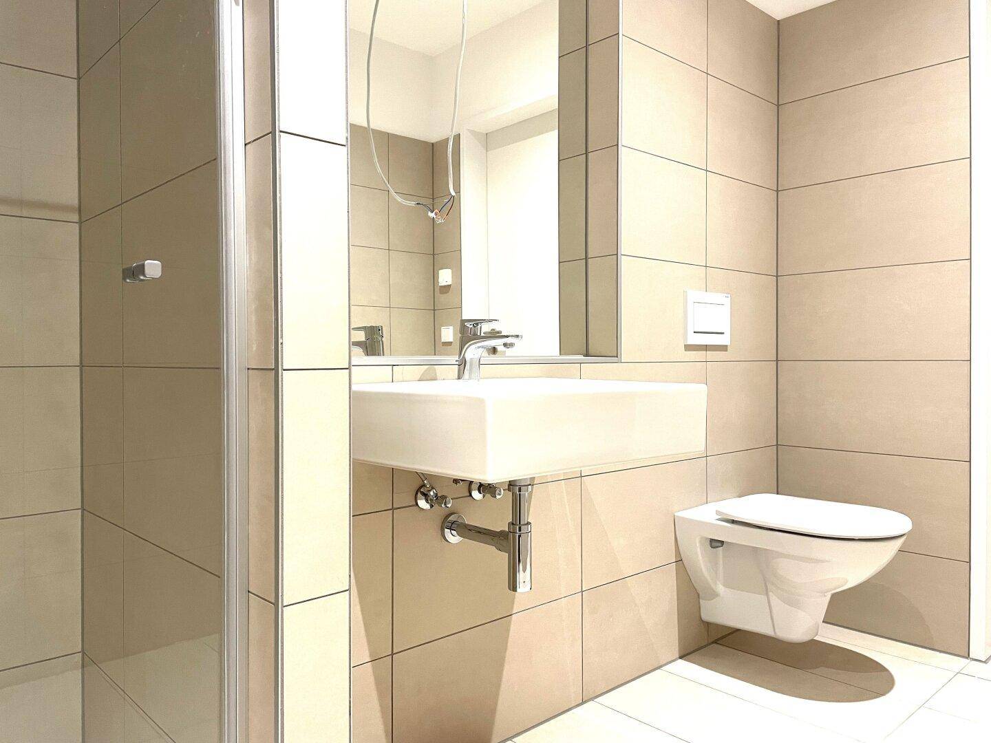 Helles Badezimmer mit beigefarbenen Fliesen, modernem Waschbecken und Toilette.