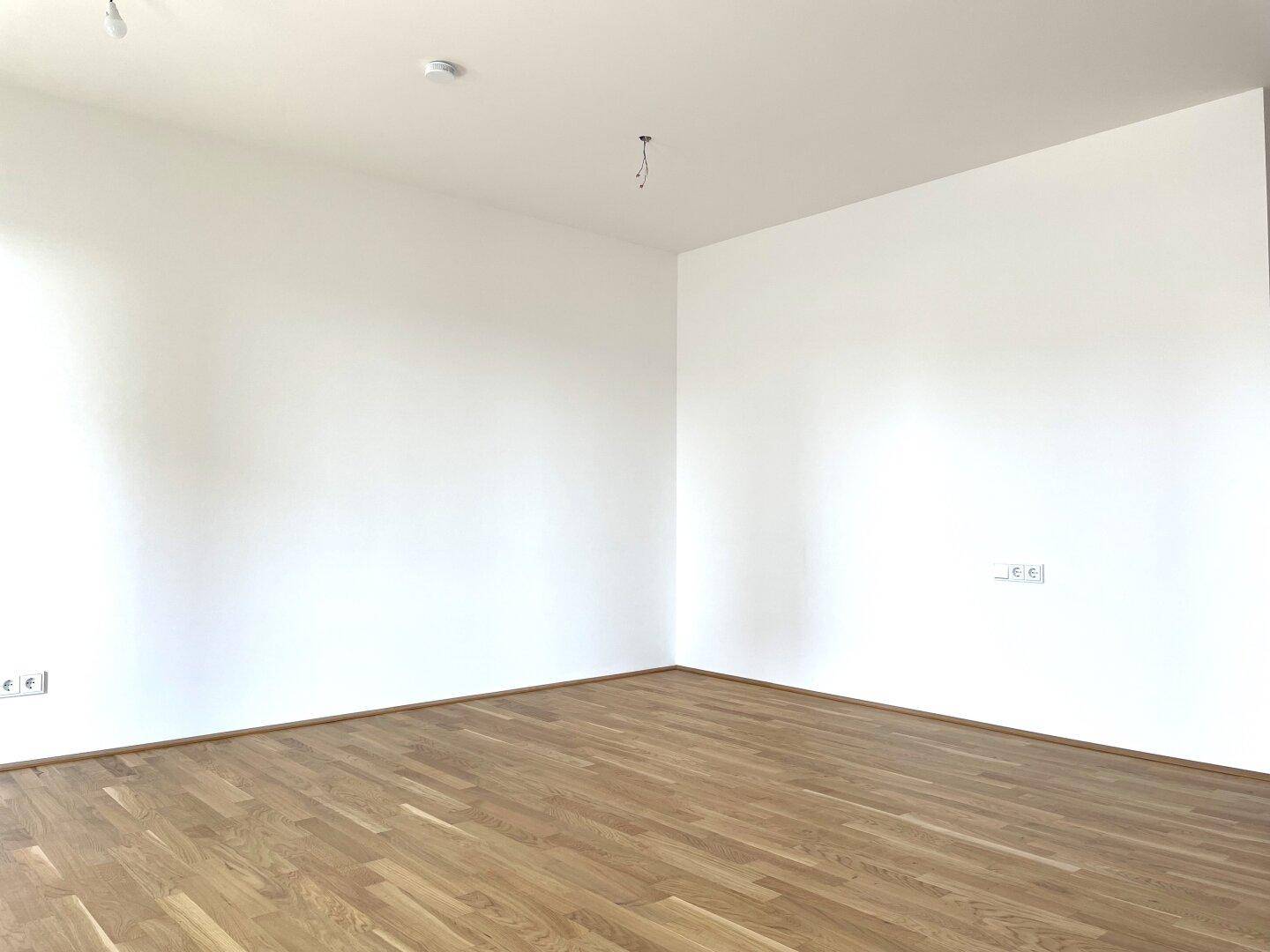 Geräumiges, leeres Zimmer mit hellem Parkettboden und weißen Wänden.