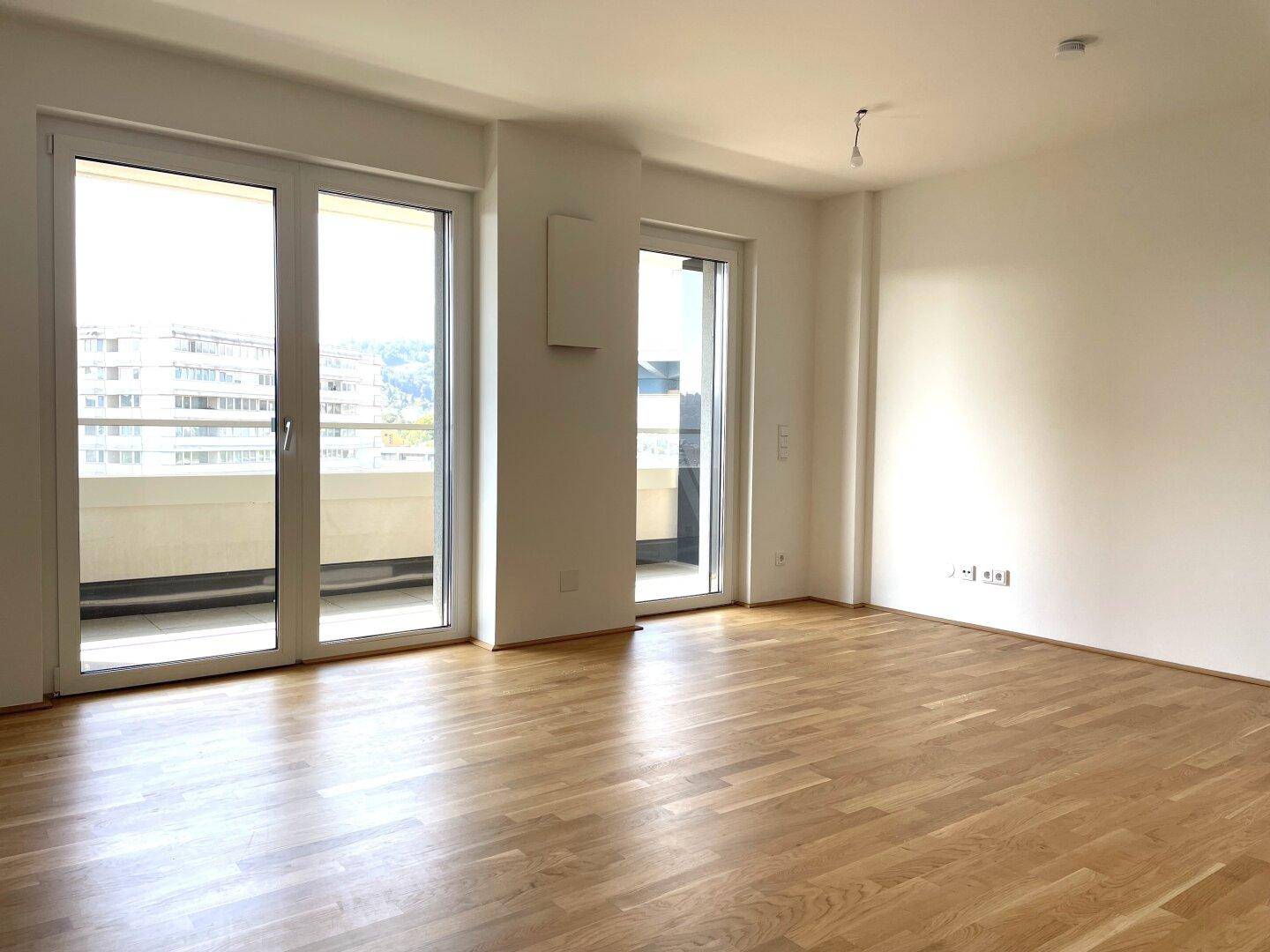 Großes, helles Zimmer mit Parkettboden und mehreren Fenstertüren zum Balkon.