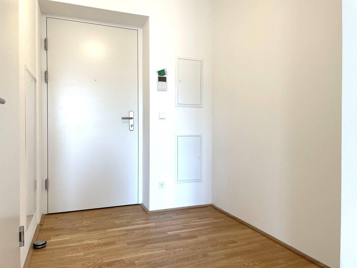 Eingangsbereich mit weißer Tür und hellem Parkettboden.