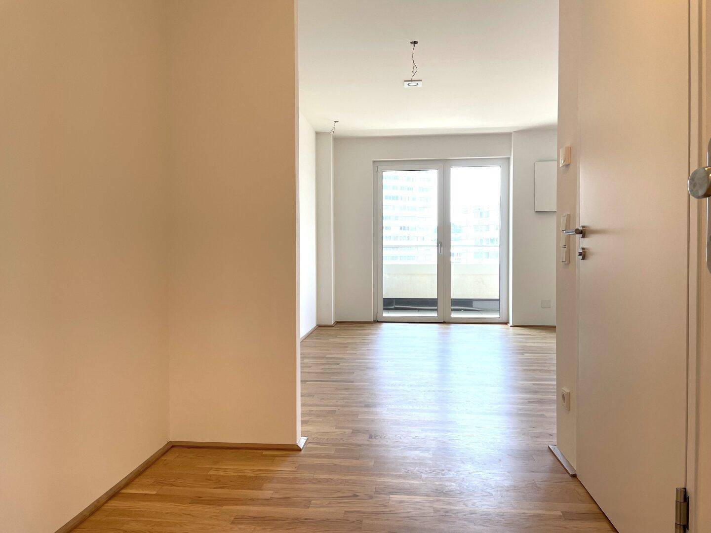 Flur mit Parkettboden und Blick in einen hellen Wohnbereich mit Balkonzugang.
