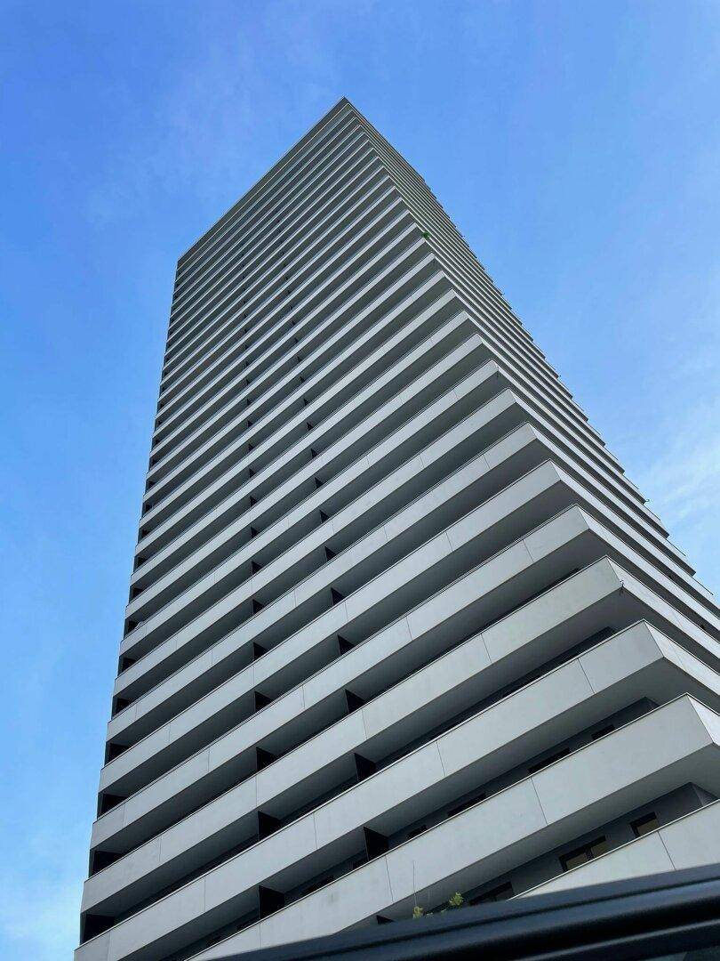 Beeindruckende Fassade eines modernen Hochhauses mit zahlreichen Balkonen unter blauem Himmel.