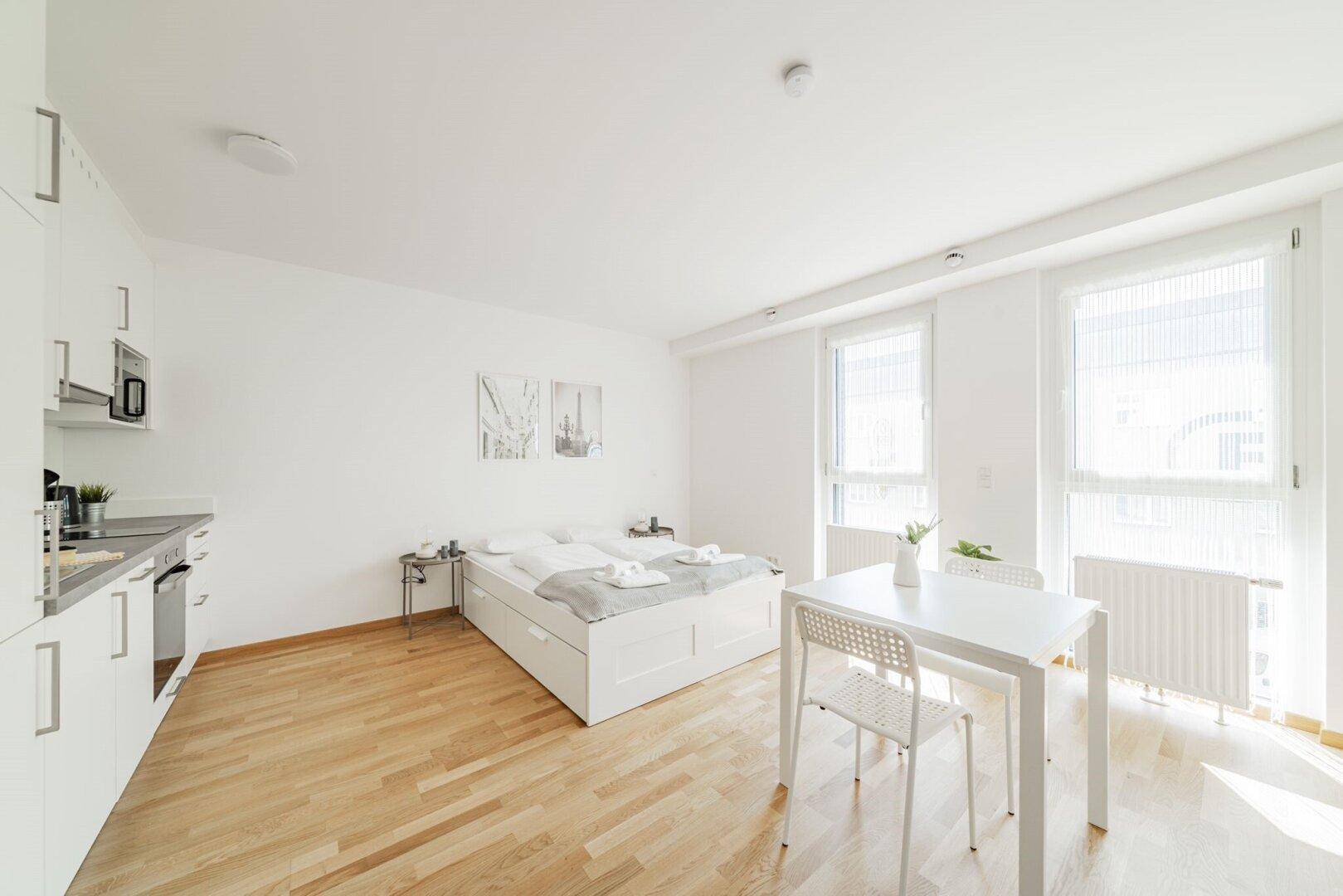 Modernes Studio-Apartment mit integrierter Küchenzeile, Bett und Essbereich.