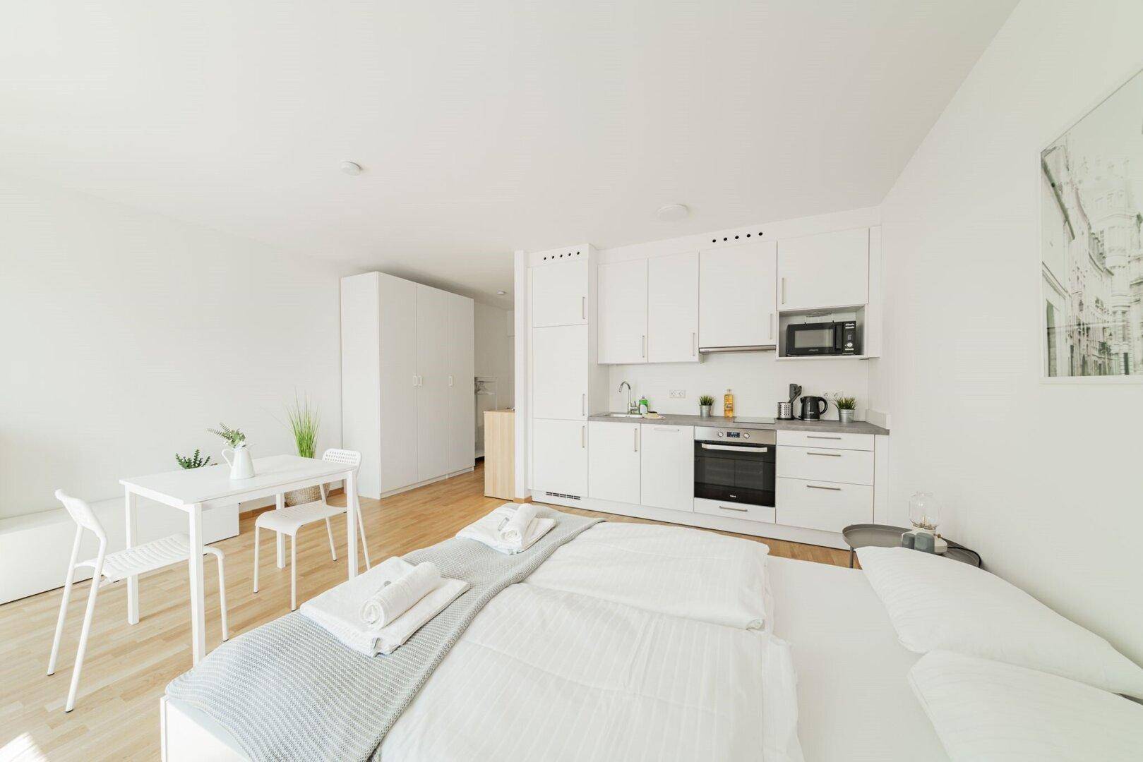 Gemütliches Studio-Apartment mit Bett, Essbereich und kompakter Küchenzeile.