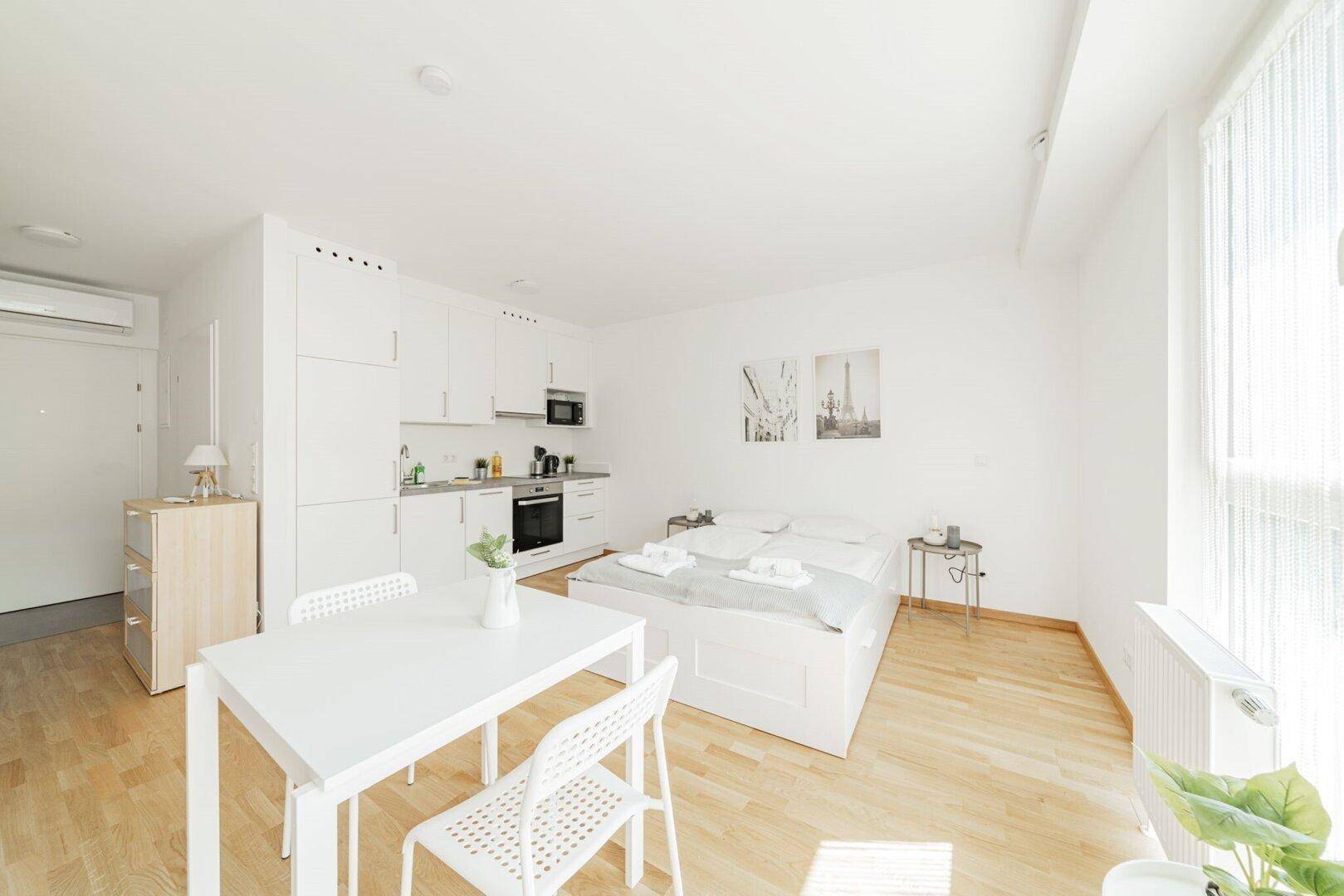 Modernes Studio-Apartment mit integrierter Küchenzeile, Bett und Essbereich.