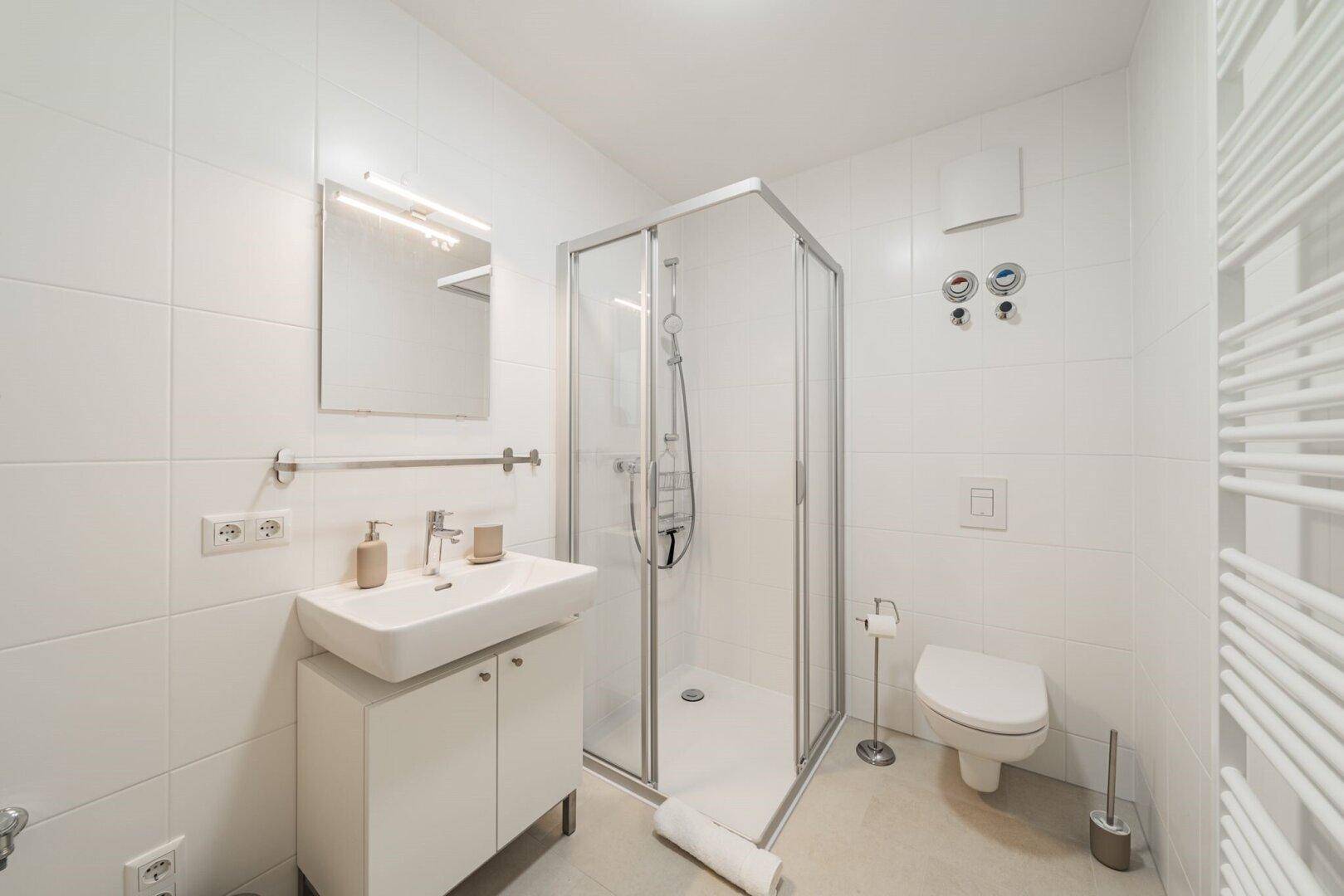 Modernes Badezimmer mit Duschkabine, WC, Waschbecken und Handtuchheizkörper.