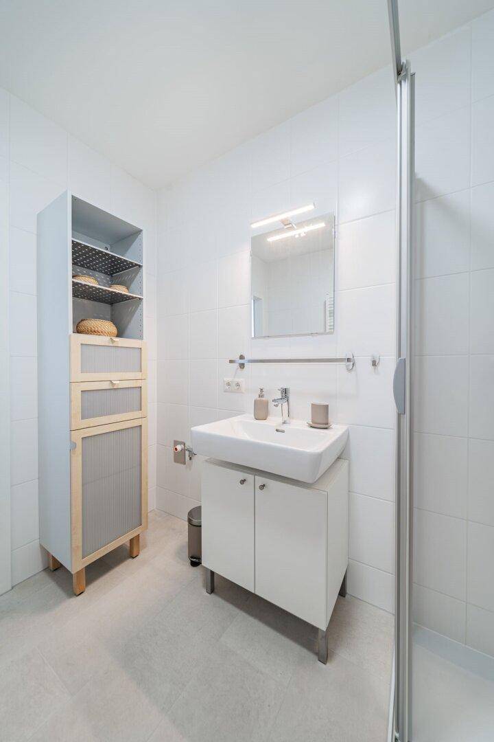 Funktionales Badezimmer mit Duschkabine, Waschbecken und praktischem Hochschrank.