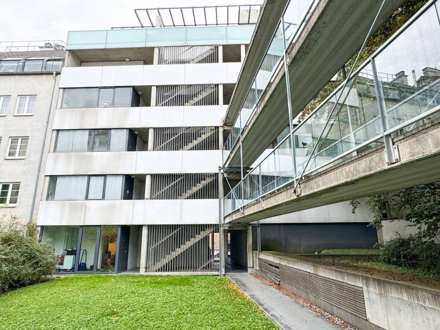 Moderne Gebäudefassade mit Glasbrücke und Grünflächen im Vordergrund.