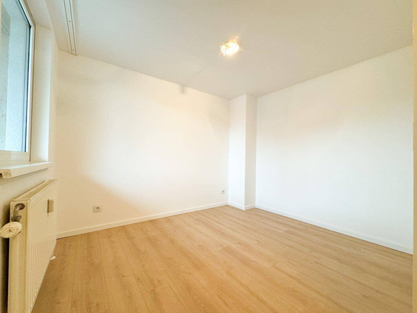 Leeres Zimmer mit hellem Laminatboden und Fenster, bereit zur individuellen Gestaltung.