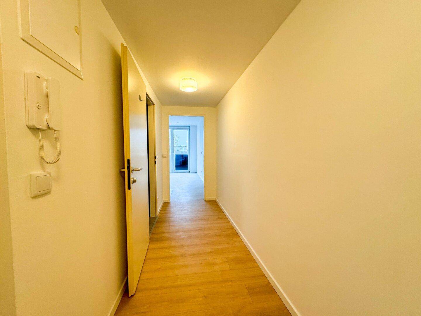Heller Flur mit Laminatboden und Gegensprechanlage, der zu weiteren Räumen führt.