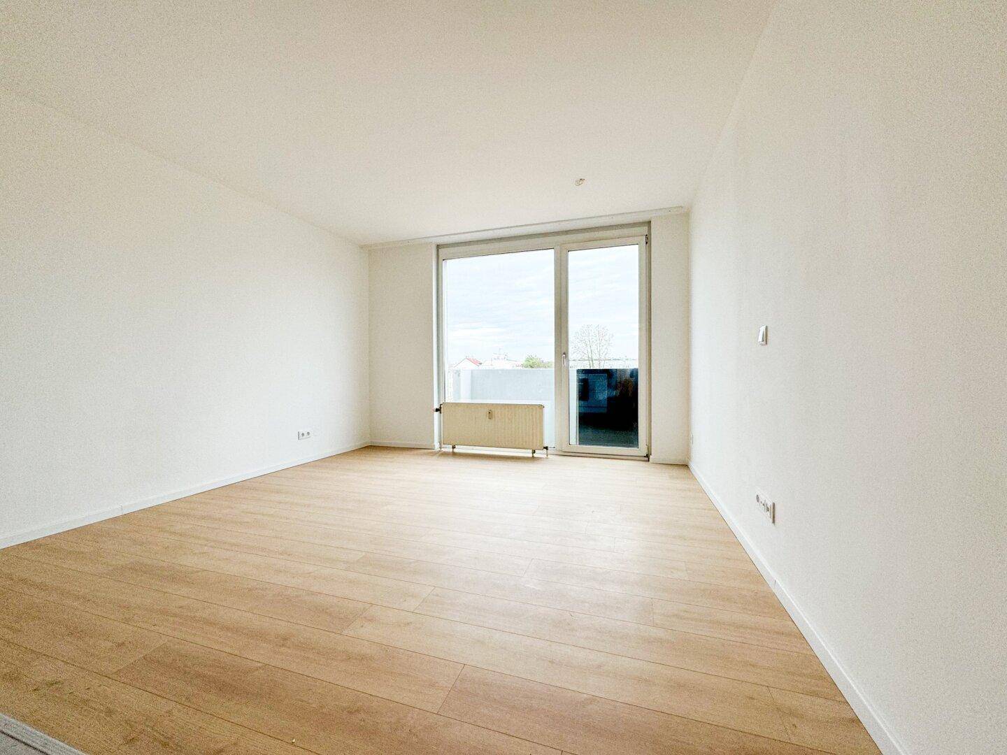 Helles Wohnzimmer mit großem Fenster und Zugang zu einem möglichen Balkon.
