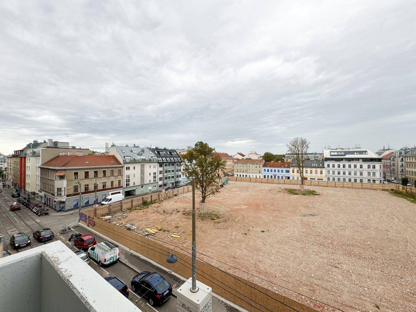 Weitläufiger Blick über eine städtische Baustelle mit umliegenden Gebäuden.