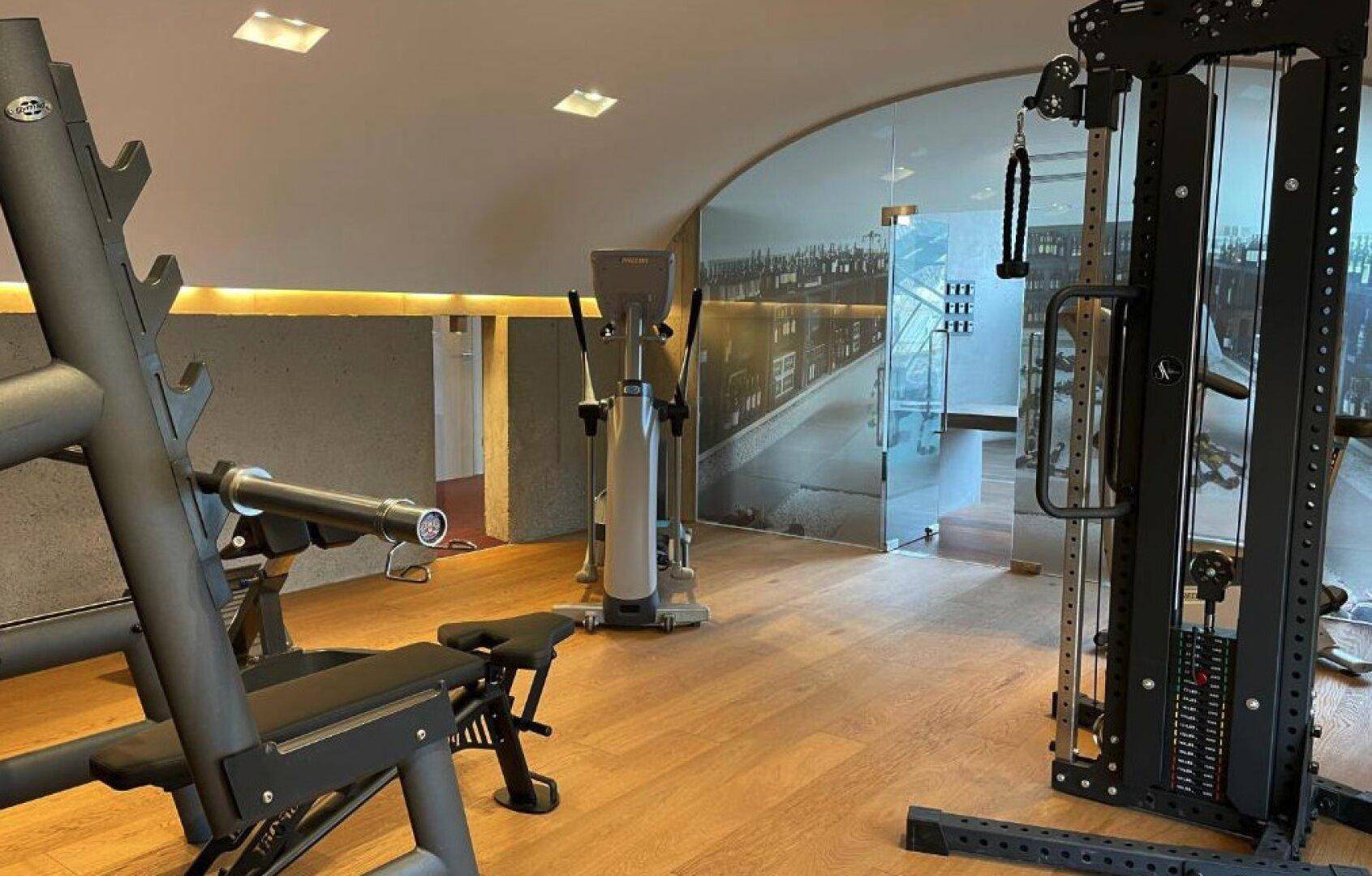 Moderner Fitnessraum mit verschiedenen Trainingsgeräten und Holzboden.