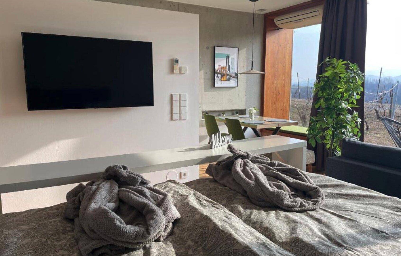 Komfortables Schlafzimmer mit großem Bett, Wandfernseher und Blick auf die Landschaft.