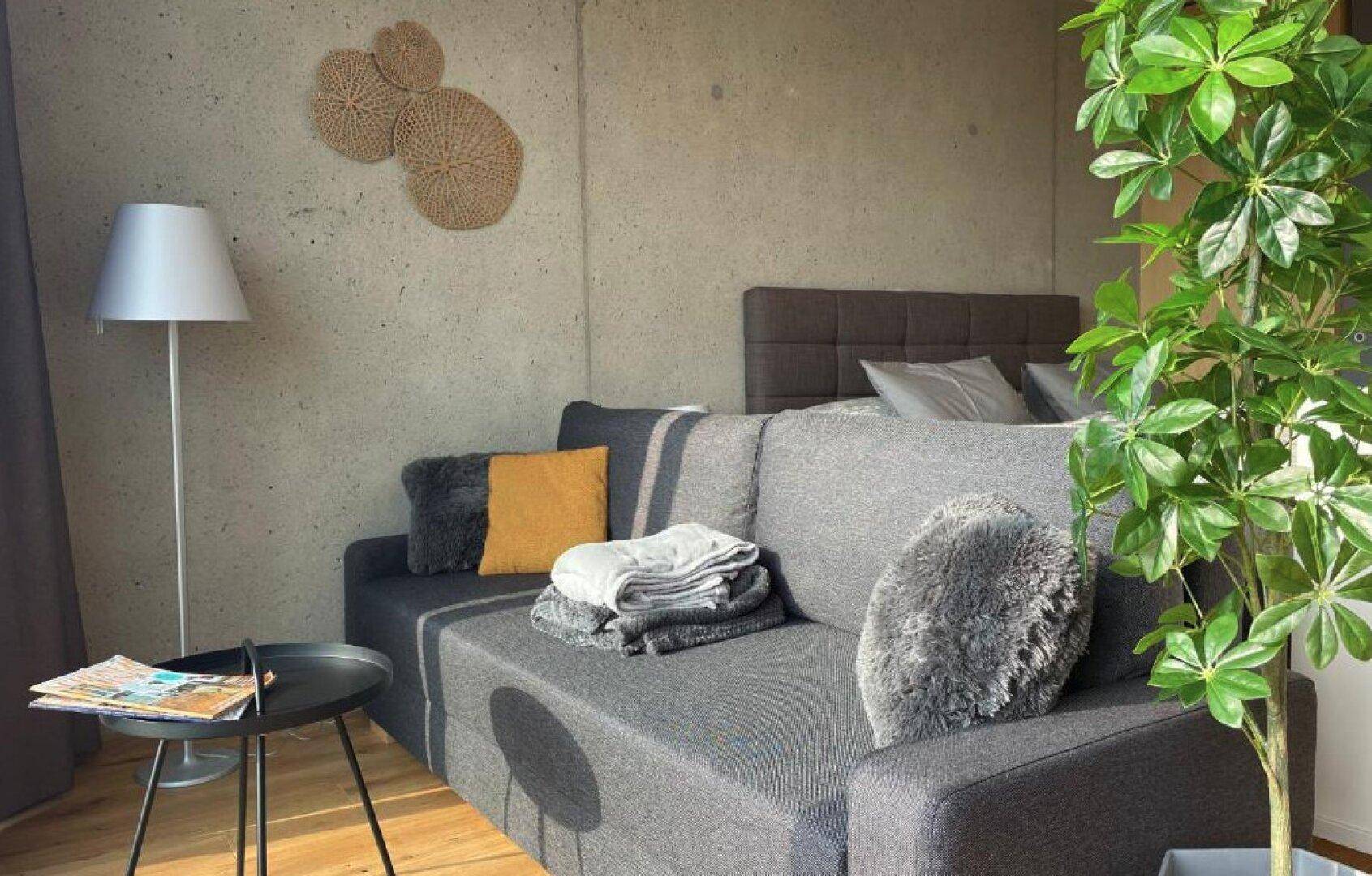 Gemütlicher Wohnbereich mit Sofa, Stehlampe und dekorativer Pflanze.