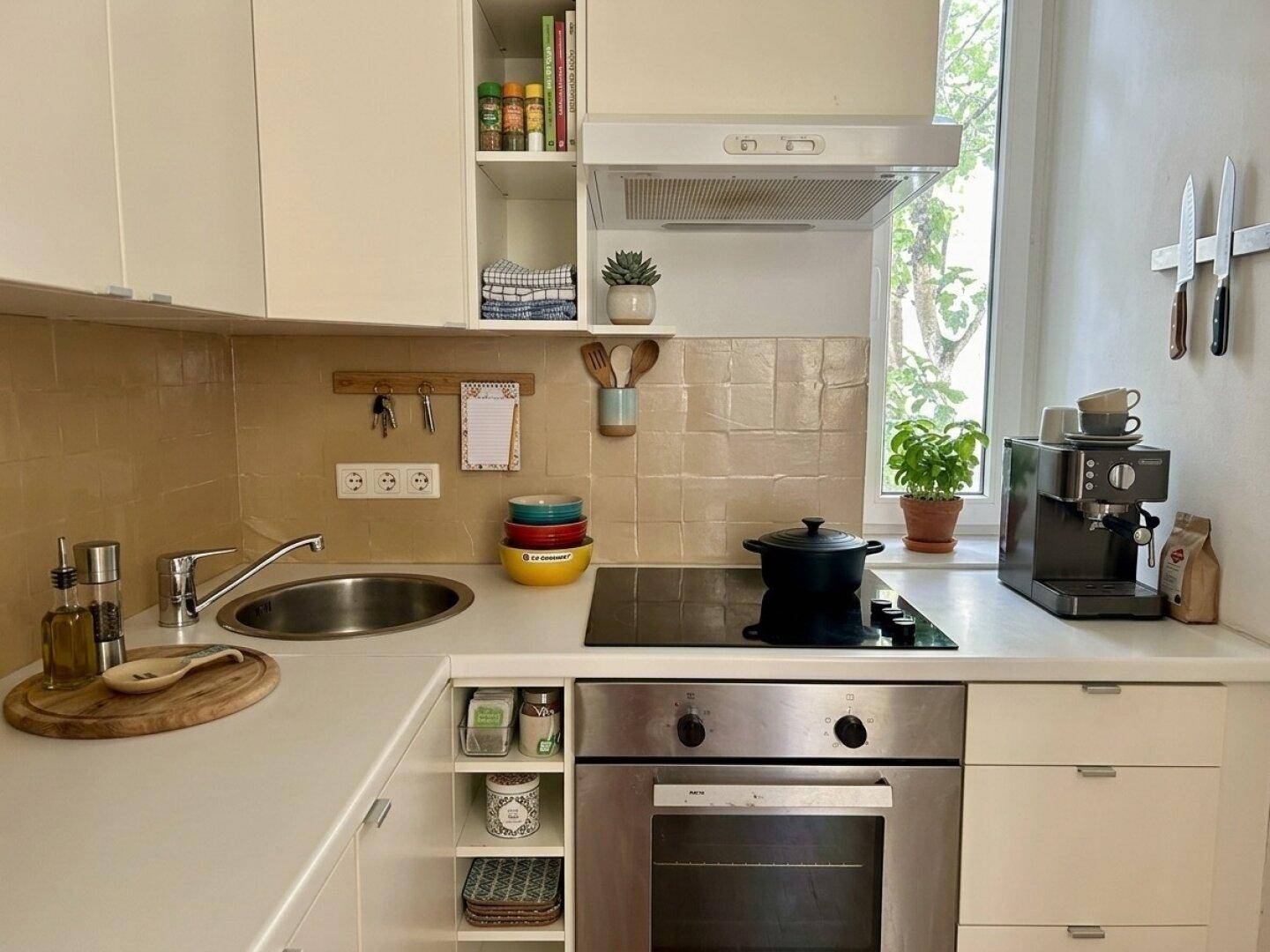 Kompakte Küche mit weißen Schränken, Induktionskochfeld und Fenster.