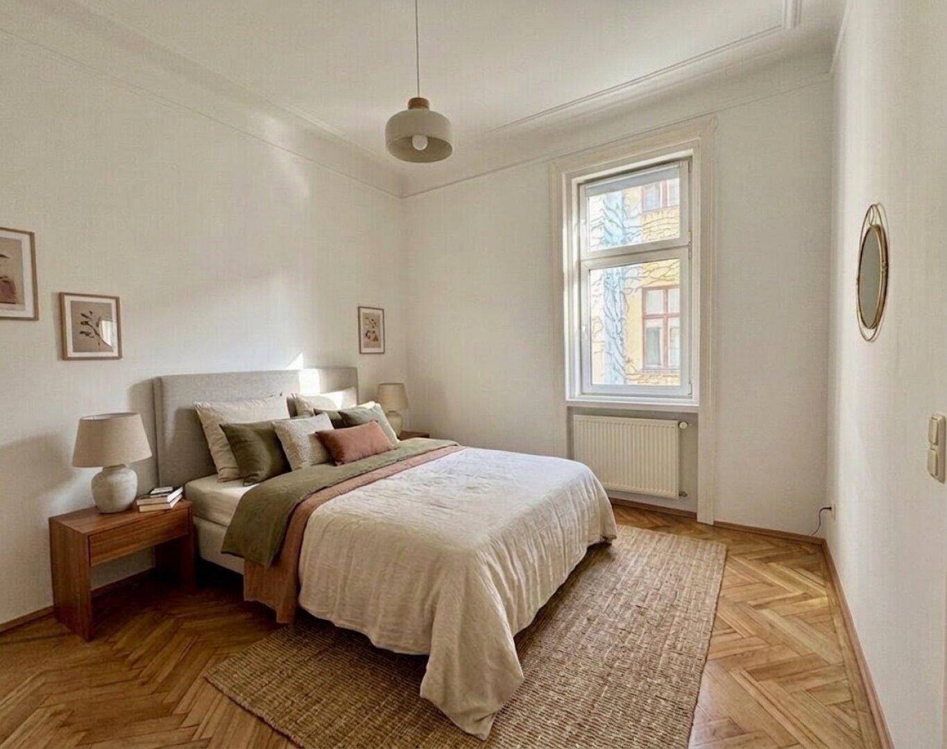 Helles Schlafzimmer mit Fischgrätparkett, großem Fenster und modernem Bett.