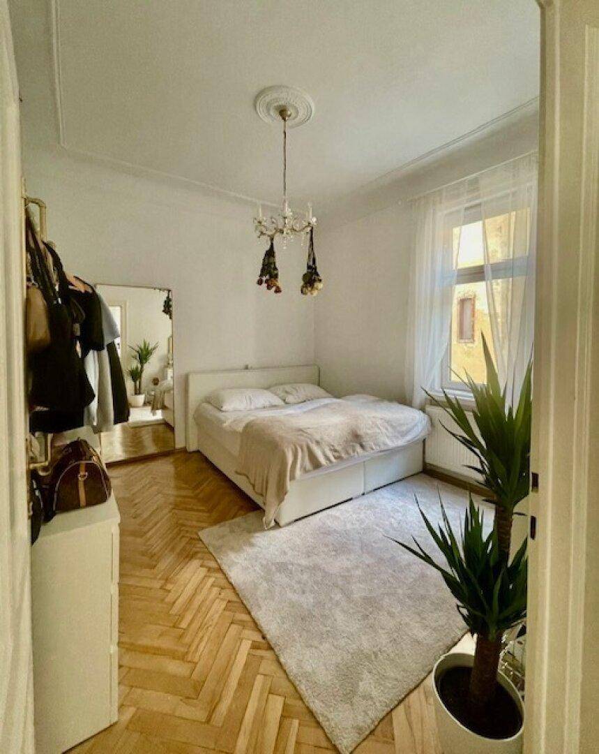 Helles Schlafzimmer mit Fischgrätparkett, großem Spiegel und Kronleuchter.