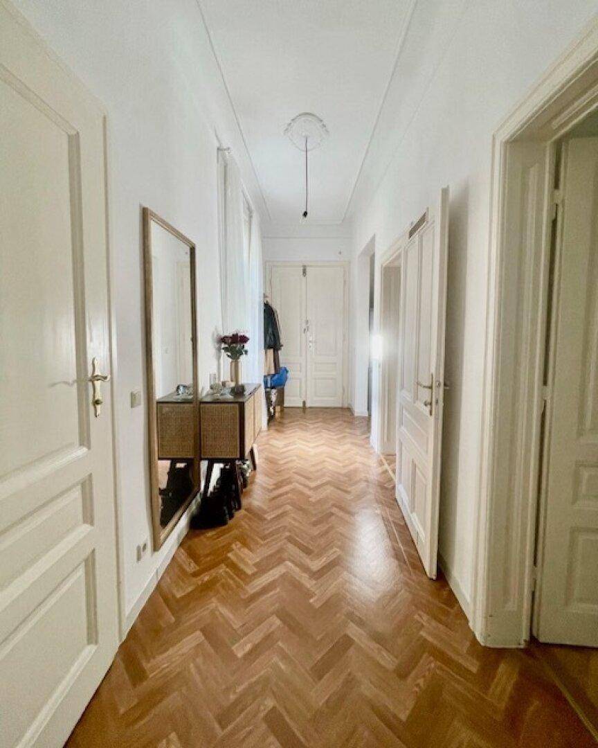 Langer Flur mit Fischgrätparkett, hohen Decken und Spiegelschrank.