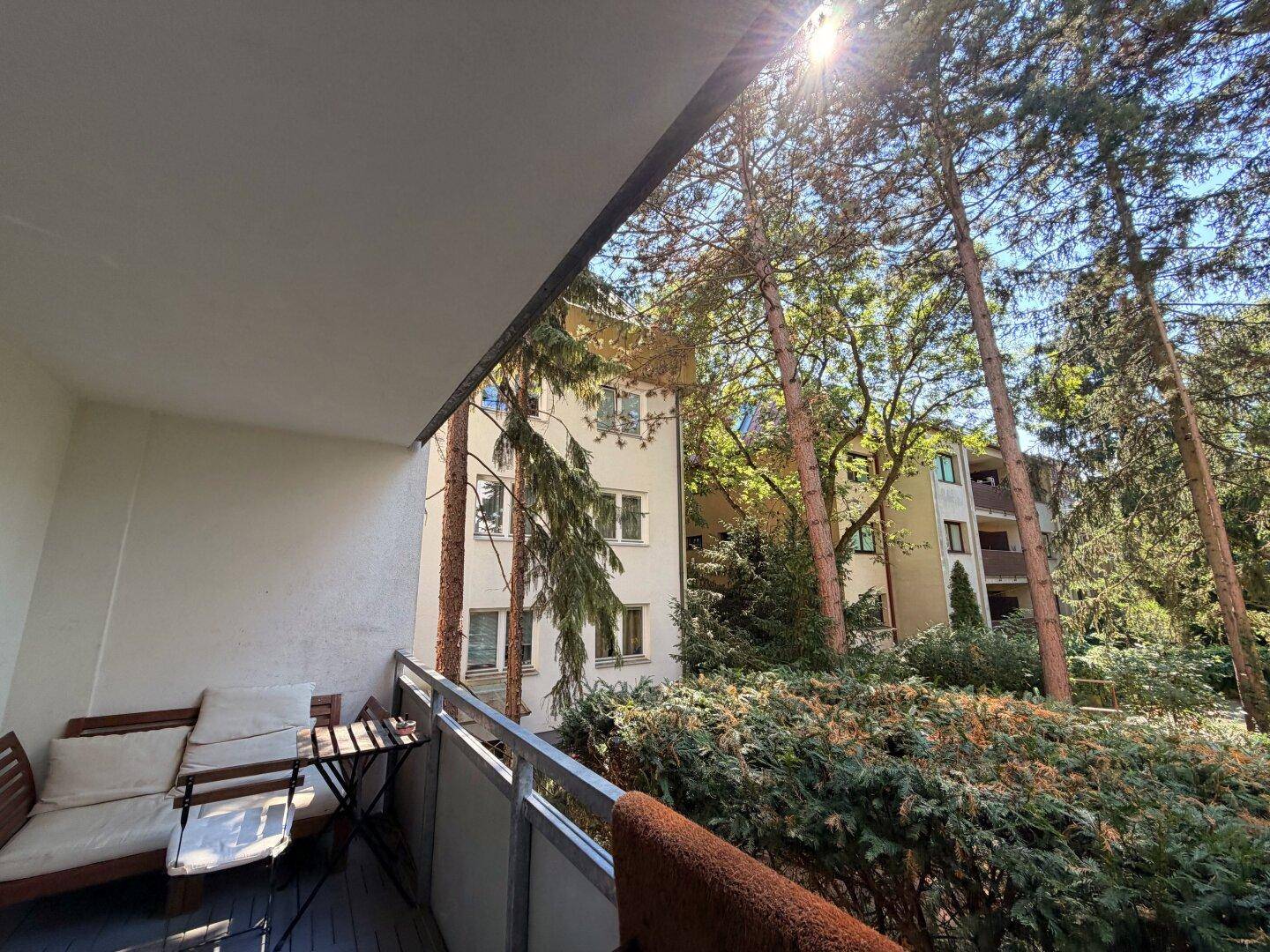 Sonniger Balkon mit Blick auf grüne Bäume und umliegende Gebäude, ideal zum Entspannen.