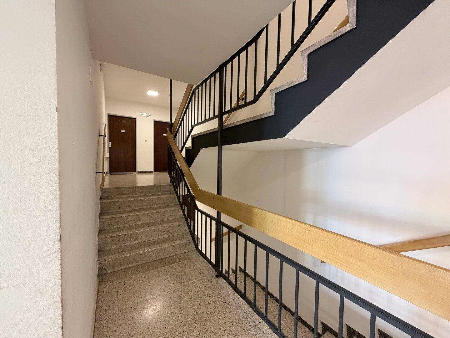 Treppenhaus mit Terrazzoboden und schwarzem Metallgeländer in einem Mehrfamilienhaus.