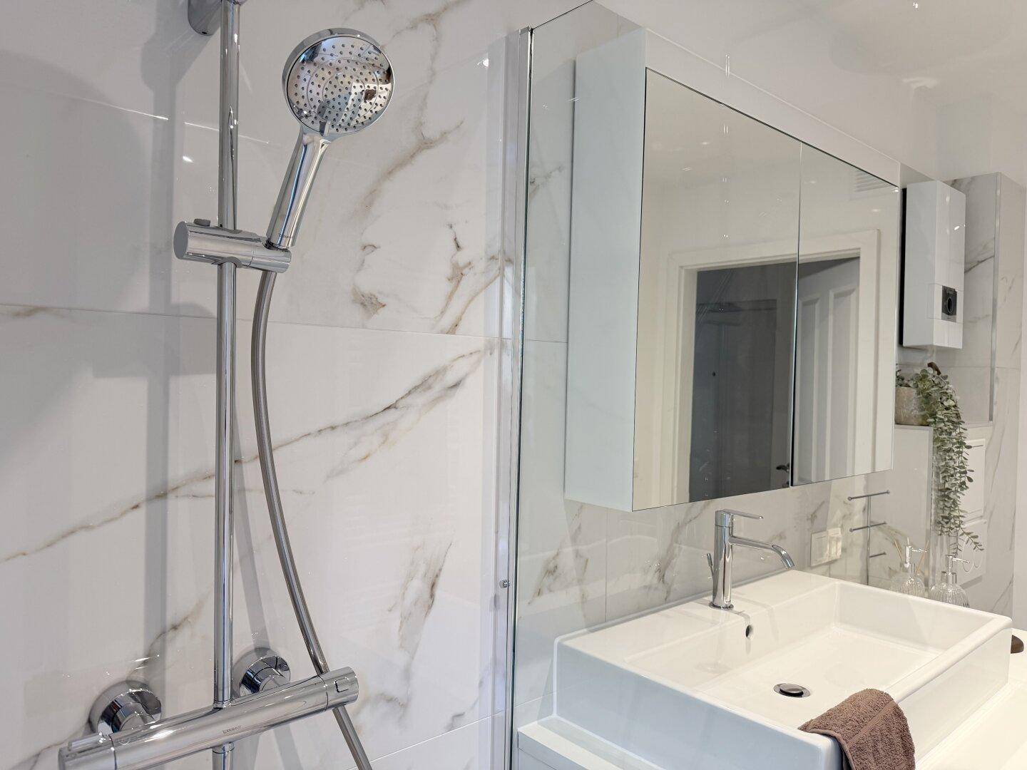 Detailaufnahme der modernen Dusche und des Waschtischs mit Marmorfliesen im Badezimmer.