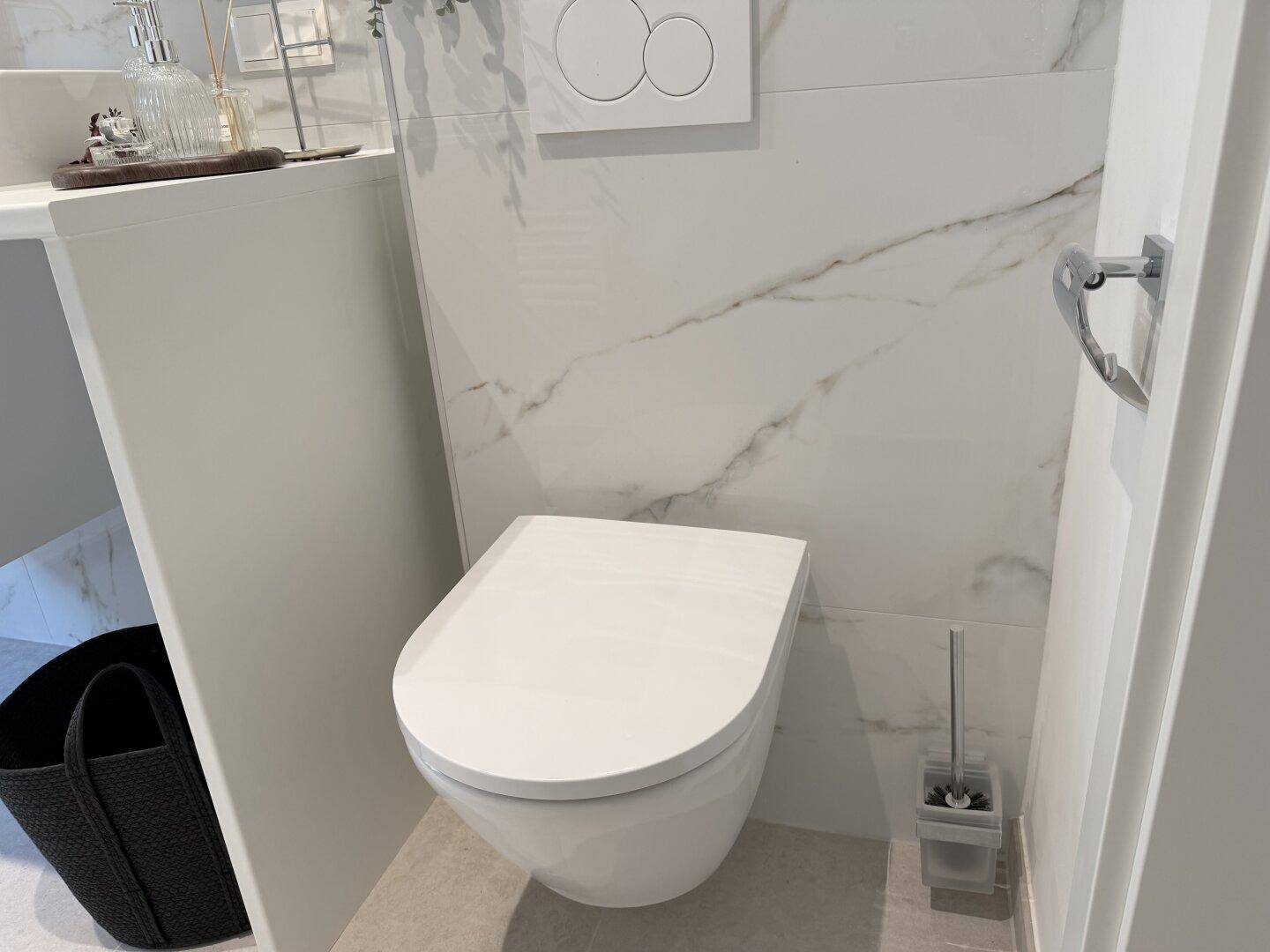 Moderne Wandtoilette mit Spülkasten und Marmorfliesen im Badezimmerbereich.