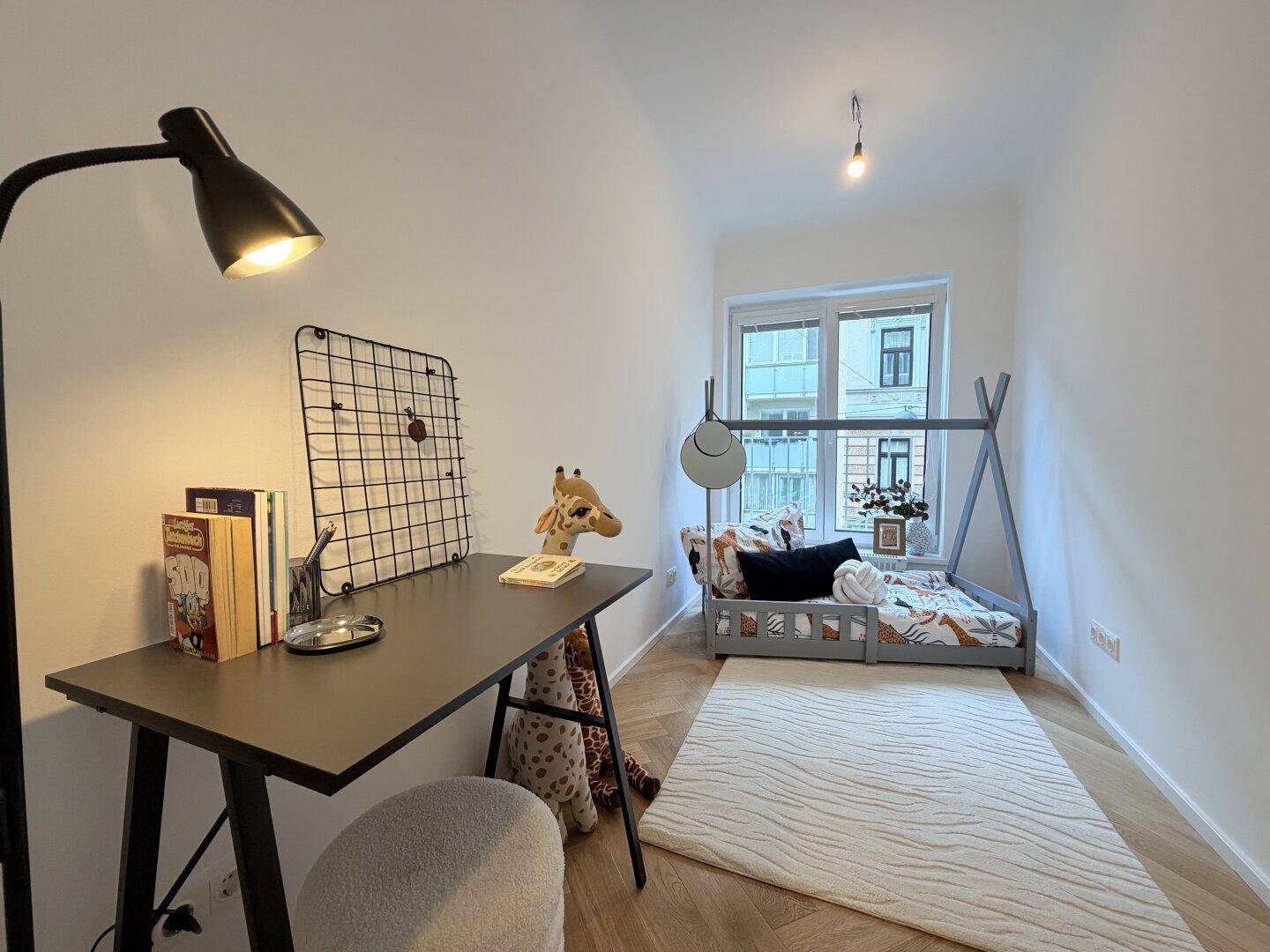 Freundliches Kinderzimmer mit Schreibtisch, Spielzeug und großem Fenster, ideal für kleine Bewohner.