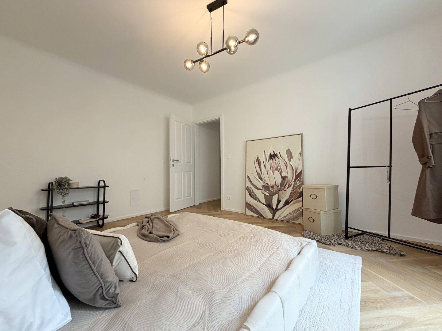 Schlafzimmer mit modernem Bett, offener Kleiderstange und Kunstwerk an der Wand.