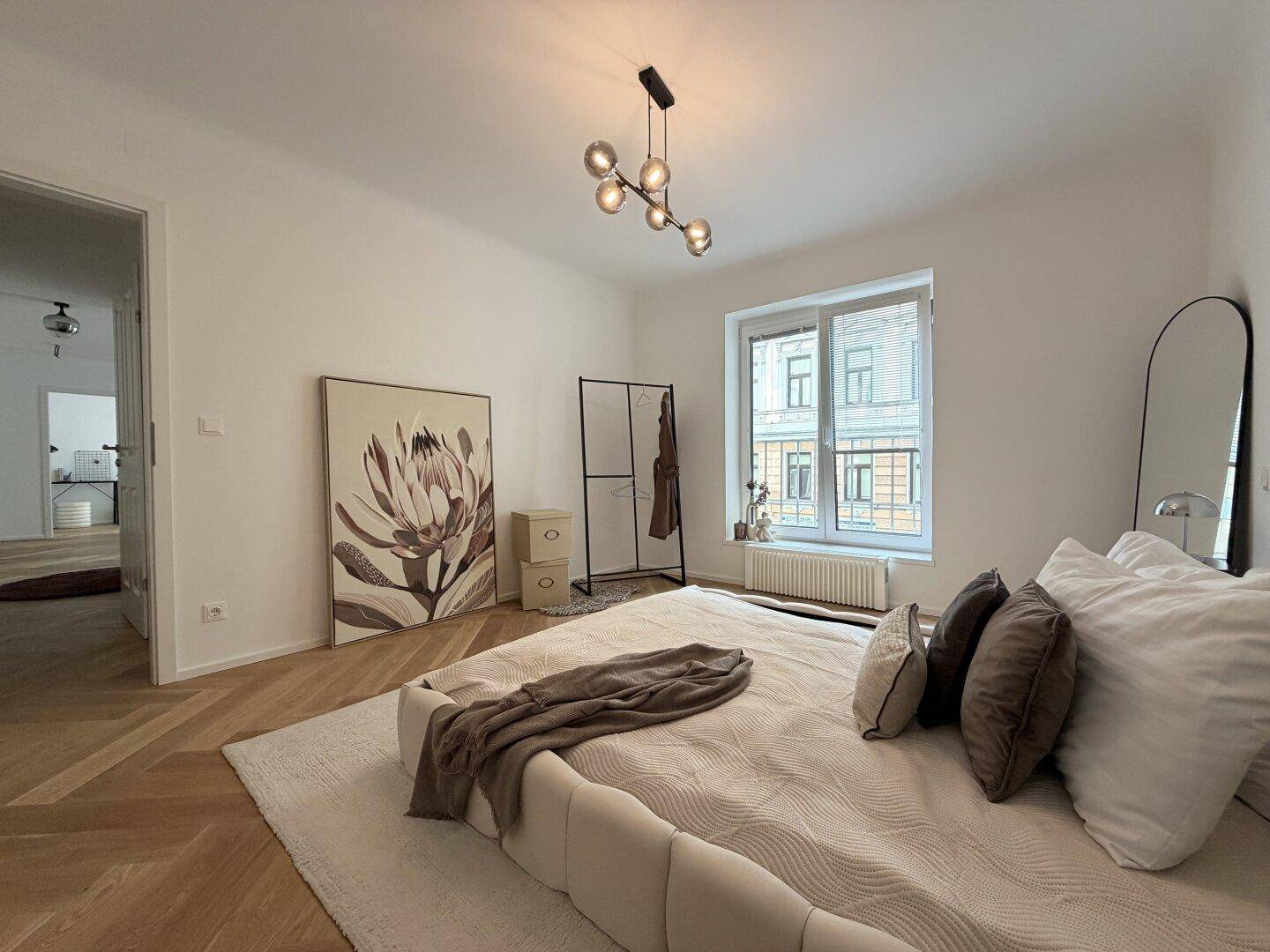 Helles Schlafzimmer mit großem Fenster, modernem Bett und Fischgrätparkett, einladend gestaltet.