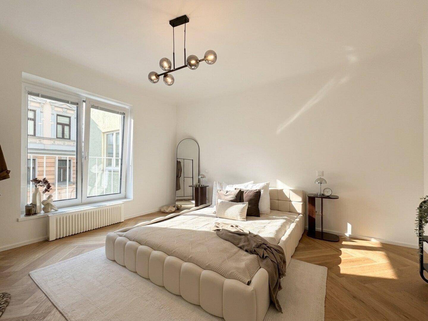 Helles Schlafzimmer mit modernem Bett, Fischgrätparkett und großem Fenster für viel Tageslicht.