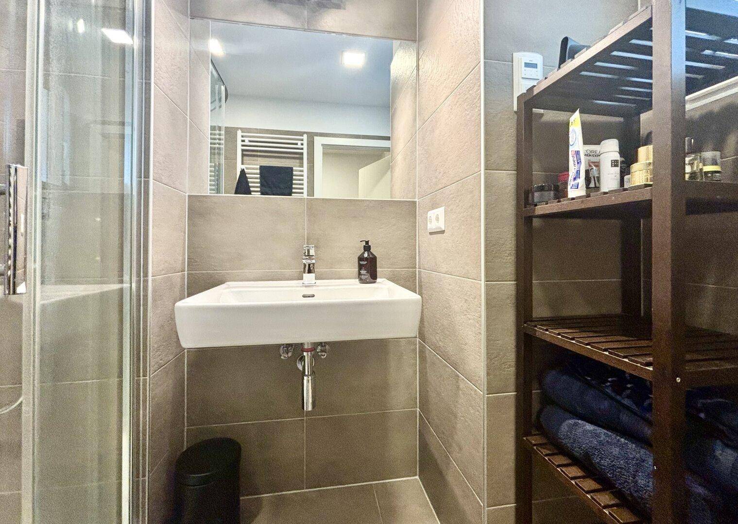 Modernes Badezimmer mit Waschbecken, Spiegel und Duschkabine.