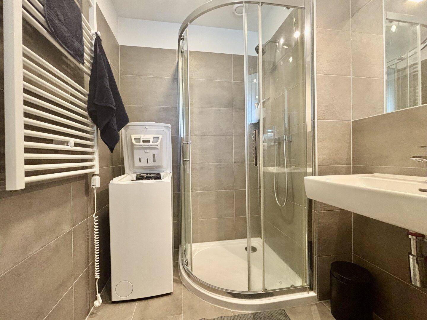 Badezimmer mit Duschkabine, Waschmaschine und beheiztem Handtuchhalter.