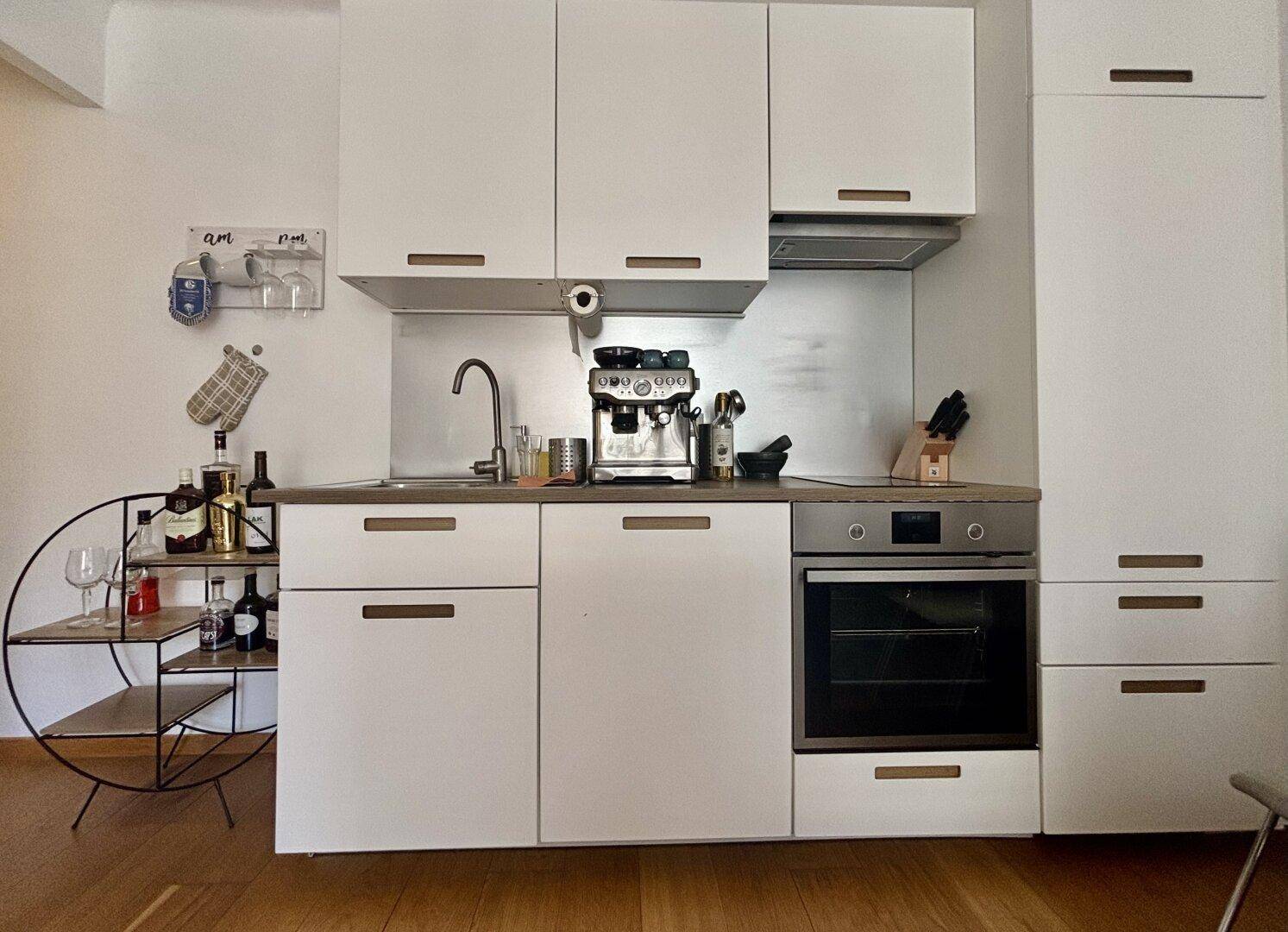 Moderne Küchenzeile mit weißen Schränken, integriertem Backofen und Kaffeemaschine.