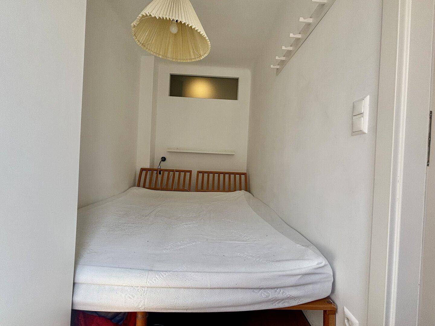 Kleiner Schlafbereich mit Bett und minimalistischer Einrichtung.