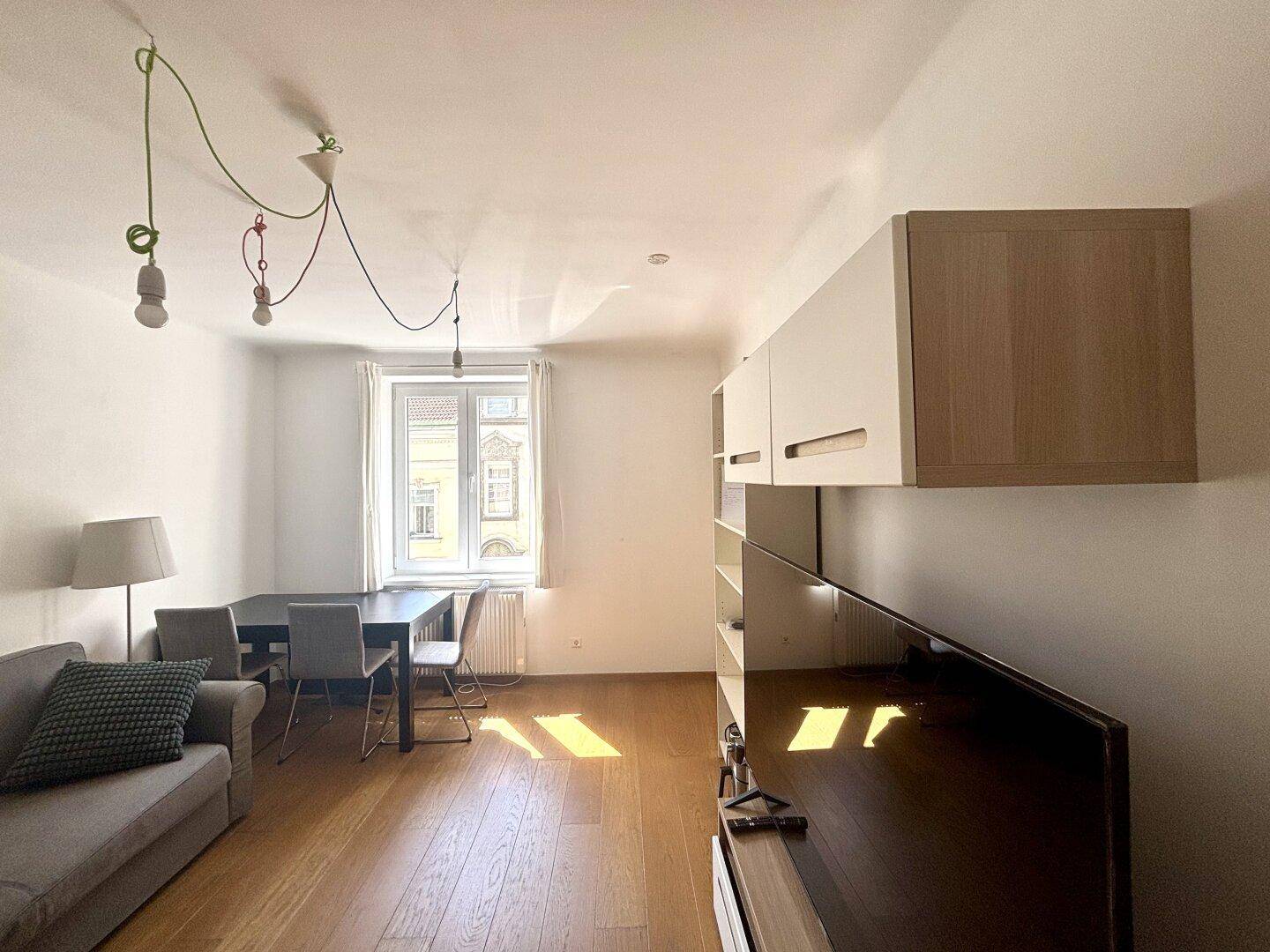 Wohn-Essbereich mit Sofa, Esstisch und Wandregal, durchflutet von natürlichem Licht.