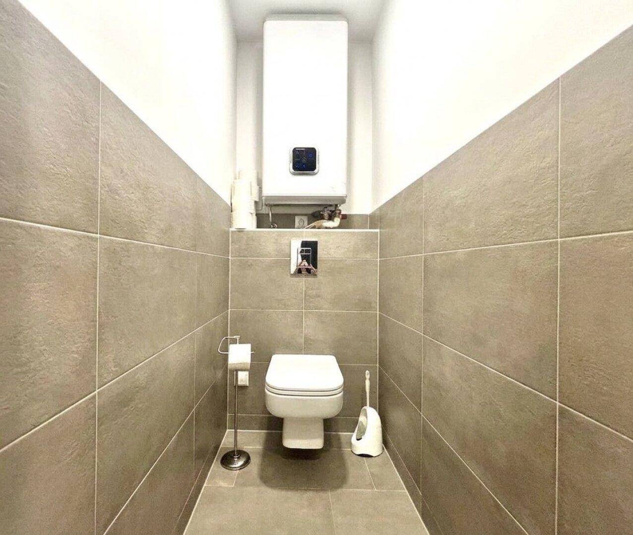 Separates WC mit Wand-WC, Fliesen und Warmwasserboiler.