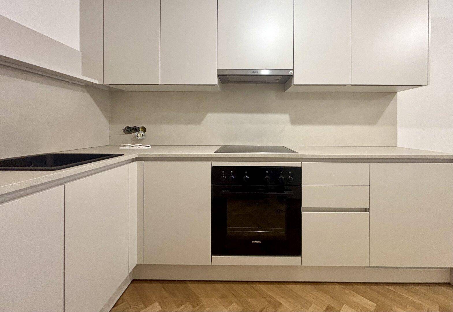 Moderne Einbauküche mit hellen Schränken, Induktionskochfeld und integriertem Backofen.